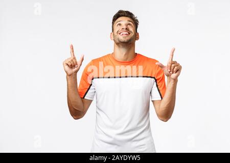 Un homme à la belle barbe stupéfié et enchanté dans un t-shirt sportif, se lève la tête et se montre étonné, souriant du bonheur et du JO Banque D'Images