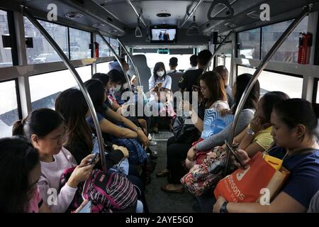 Mandaluyong City, Philippines - 13 février 2020: Les passagers utilisent leur smartphone pour passer le temps tout en conduisant un mini-bus. Banque D'Images
