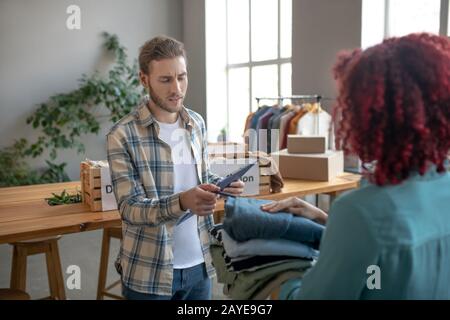 Jeune homme écrivant dans un carnet, près d'une femme avec des vêtements dans les mains. Banque D'Images