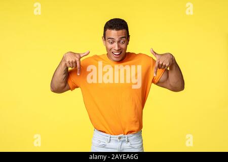 Excité bon-look beau gars hispanique masculin, porter un t-shirt orange, pantalon blanc, soulever les sourcils de l'étonnement et impres Banque D'Images