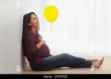 Femme enceinte pensant à son bébé et souriant avec un ballon dans sa main. Banque D'Images