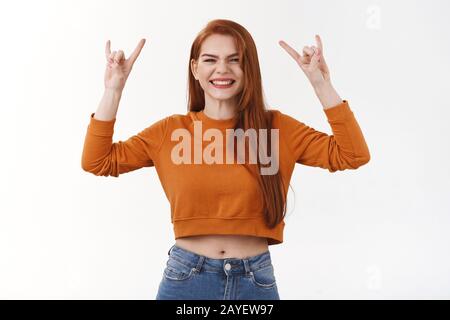 Une jeune fille à la tête rouge qui se sent surjoy assister à un concert impressionnant, se lève les mains sur le rock-n-roll, signe de métal lourd et se sent gâtée du plaisir et de la joie Banque D'Images