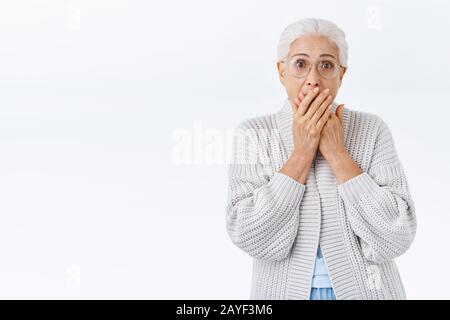 Une grand-mère choquée et effrayée qui s'inquiète pour son enfant, stupéfiante car un membre de sa famille a eu des ennuis, regardant la télévision d'informations terrifiante, se couvrir la bouche Banque D'Images