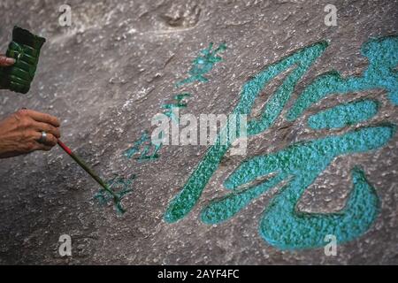 Homme peindre des personnages chinois de calligraphie sur un rocher Banque D'Images