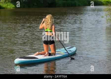 Femme caucasienne palettes avec SUP sur l'eau Banque D'Images