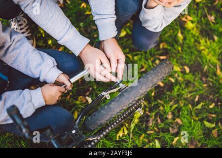 Fête des pères. Un grand père de famille sympathique et des fils ensemble se détendent activement dans l'air frais. Papa enseigne aux fils de réparer la bicyclette Banque D'Images