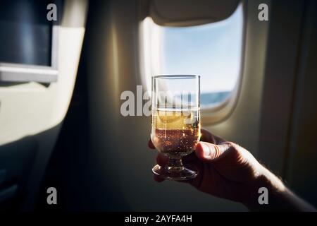 Dring pendant le vol. Homme tenant un verre de vin mousseux contre la fenêtre d'avion. Banque D'Images