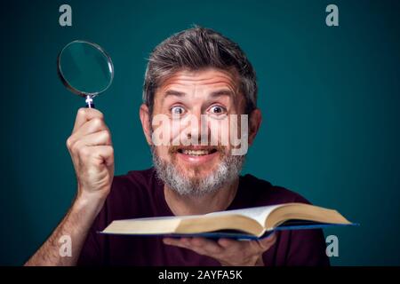 Un portrait d'homme barbu dans un t-shirt rouge tenant un livre ouvert et une loupe. Concept de personnes, d'éducation et de recherche Banque D'Images