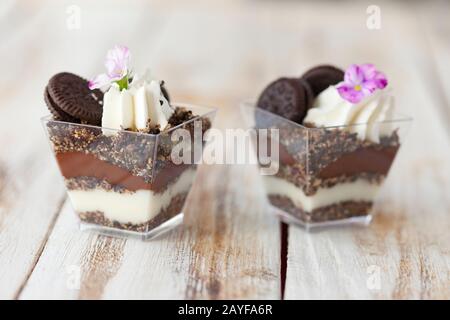 Trifle chocolat noir et blanc avec cookie. Décoré avec une fleur sur fond blanc vieux bois. Dessert sucré traditionnel anglais . Banque D'Images