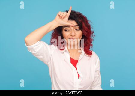 Je suis perdant! Portrait d'une femme hipster déprimée malheureuse avec des cheveux rouges fantaisie montrant le signe L sur le front, faisant le geste perdant et se sentant non sécurisé, disa Banque D'Images