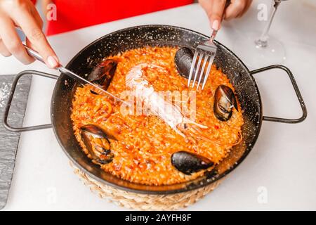 Femme mangeant de la paella espagnole traditionnelle avec fruits de mer et riz sur la table au restaurant Banque D'Images