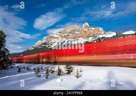 Exposition prolongée de la locomotive rouge qui passe par Castle Mountain en hiver près de Banff, Alberta, Canada Banque D'Images