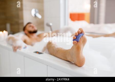 Homme allongé dans le bain avec mousse le matin Banque D'Images