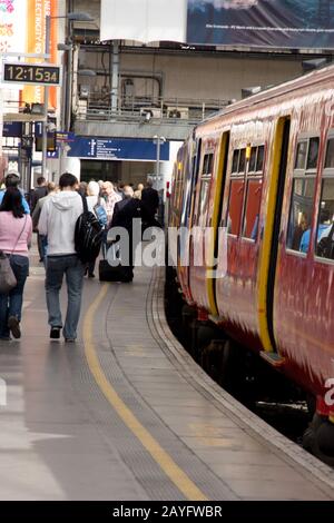 Un train de banlieue à la gare de London Waterloo avec des passagers marchant le long de la plate-forme Banque D'Images