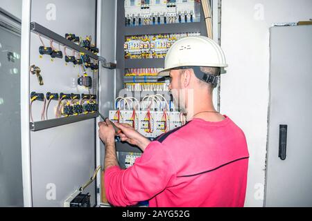 L'ingénieur d'un casque blanc travaille dans une armoire électrique. L'électricien répare le boîtier électrique. Contrôle de l'équipement de commutation du haute tension Banque D'Images