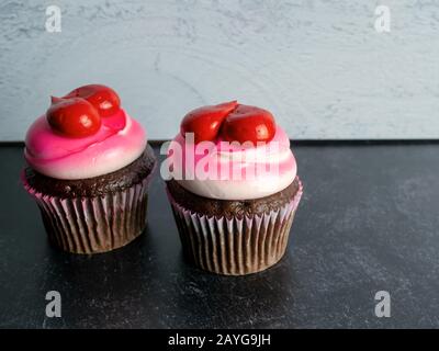 Deux cupcakes au chocolat, décorés avec une mousse blanche et rose et des coeurs rouges sur fond d'ardoise noire et de shiplap gris, parfaits pour l'amour, la Saint-Valentin Banque D'Images