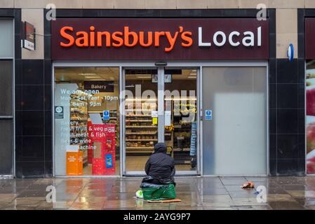 Le mendiant se cousue à la porte d'un magasin local de Sainsbury sur Morrison Street, Édimbourg, Écosse, Royaume-Uni. Banque D'Images