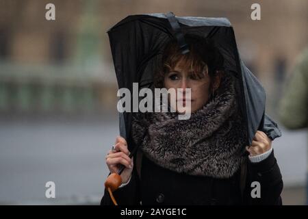 Une femme est secouée par des vents violents lorsqu'elle traverse le pont de Westminster, dans le centre de Londres, alors que Storm Dennis provoque un deuxième week-end de perturbations avec de mauvais temps qui fait des ravages à travers le Royaume-Uni. Banque D'Images