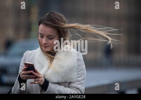 Une femme est secouée par des vents violents lorsqu'elle traverse le pont de Westminster, dans le centre de Londres, alors que Storm Dennis provoque un deuxième week-end de perturbations avec de mauvais temps qui fait des ravages à travers le Royaume-Uni. Banque D'Images