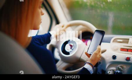 Jeune blonde femme dans sa nouvelle voiture souriant. Utilisez le smartphone dans la voiture Banque D'Images