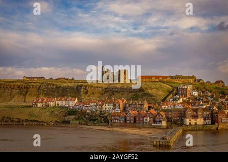 Le port extérieur de Whitby. Maisons nichées sous la falaise avec une église et l'abbaye de Whitby sur le sommet de la colline. Un ciel nuageux est au-dessus. Banque D'Images