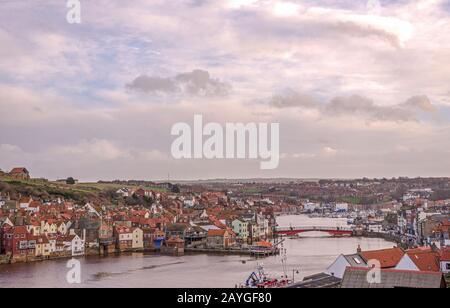 Port de Whitby et ville donnant vers l'intérieur. Les bâtiments de la ville se regroupent autour du port et un pont s'étend sur l'eau. Un ciel nuageux est au-dessus. Banque D'Images