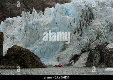 Un zodiaque avec les touristes navigue près de la chute d'eau en face du glacier Condor dans le détroit d'Agostini, Cordillera Darwin, à Tierra del Fuego in Banque D'Images