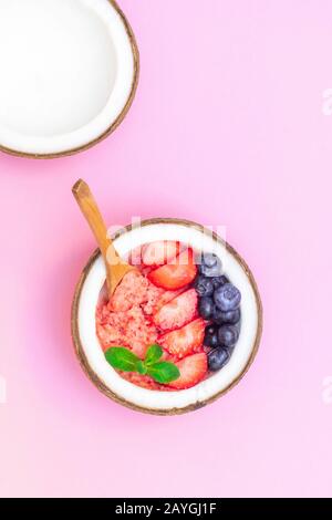 Vue de dessus du bol à noix de coco avec smoothie aux baies saines sur fond rose Banque D'Images