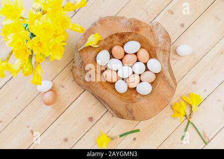 Décoration d'arrière-plan de Pâques avec œufs dans un bol en bois, feuilles vertes et cloches de Pâques, fleurs de jonquille sur parquet. Décoration de printemps. Naturellement d Banque D'Images