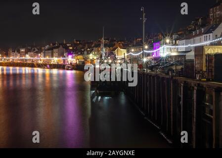 Une scène de la ville et le port de Whitby allumé jusqu'à la nuit. Les chambres lumineuses, lumières colorées se reflètent dans l'eau et un ciel sombre est ci-dessus. Banque D'Images