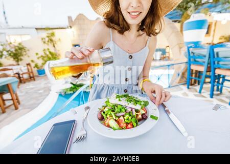 Jeune fille élégante dans le restaurant salade d'assaisonnement à l'huile d'olive. Concept de cuisine grecque et de légumes frais Banque D'Images