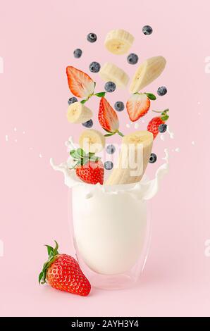 Fruits et baies d'été frais survolant le lait d'éclaboussures sur fond rose. Lévitation milkshake Banque D'Images