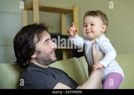 Un bébé heureux joue avec le père sur le canapé à la maison. Bébé pointe son doigt. Banque D'Images