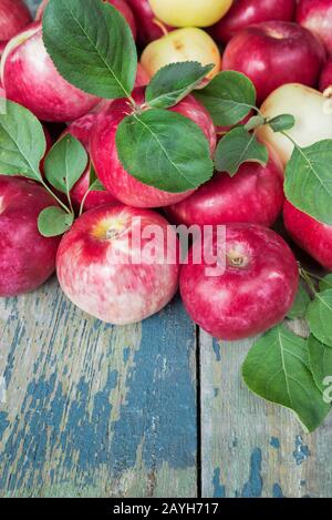 Beaucoup de pommes rouges avec des feuilles vertes sont sur l'ancienne table en bois avec place pour le texte Banque D'Images