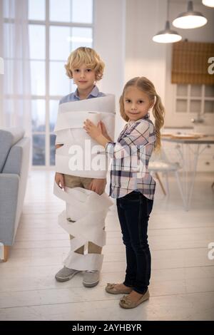 Deux enfants jouant au jeu de momie en papier toilette dans la cuisine Banque D'Images