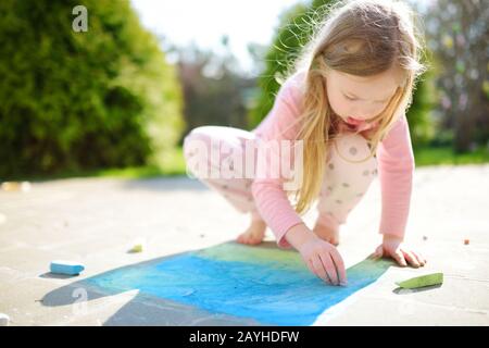 Cute little girl dessiner avec les craies colorées sur un trottoir. L'activité d'été pour les petits enfants. Loisirs créatifs pour la famille. Banque D'Images