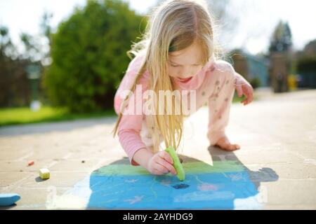 Cute little girl dessiner avec les craies colorées sur un trottoir. L'activité d'été pour les petits enfants. Loisirs créatifs pour la famille. Banque D'Images