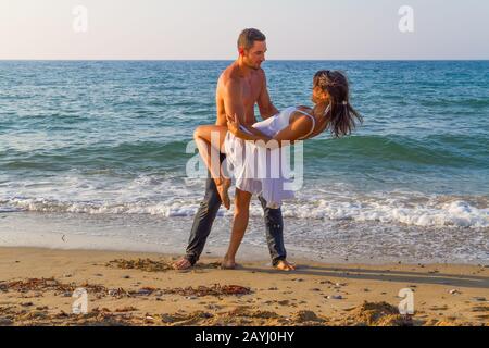 Après-midi d'été sur une plage de sable avec l'océan en arrière-plan, un jeune couple pratique une scène de danse. Banque D'Images