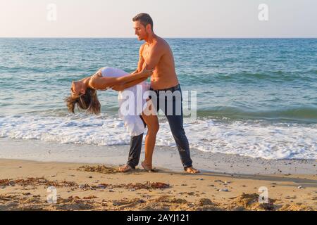 Après-midi d'été sur une plage de sable avec l'océan en arrière-plan, un jeune couple pratique une scène de danse. Banque D'Images