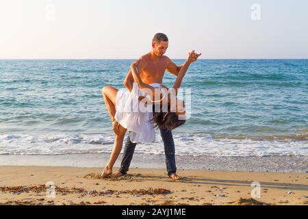 Après-midi d'été sur une plage de sable avec l'océan en arrière-plan, un jeune couple pratique une scène de danse. Banque D'Images