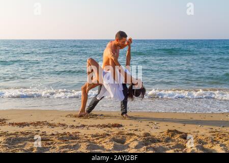 Après-midi d'été sur une plage de sable avec l'océan en arrière-plan, un jeune couple pratique une scène de danse. Banque D'Images