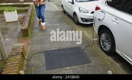 Câble de chargement pour une voiture électronique posée sur le trottoir, un tapis empêchant de trébucher, Pays-Bas Banque D'Images