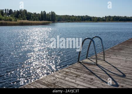 Quai de baignade en bois avec échelle en métal sur lac bleu calme journée ensoleillée sur la nature Finlande station naturelle idyllique Banque D'Images