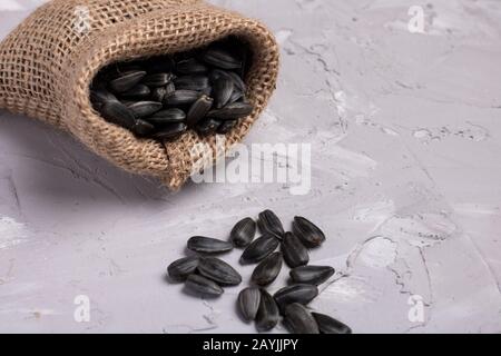 Graines de tournesol dans un sac de toile, fond gris, foyer sélectif. Graines noires dispersées à partir de burlap, zéro gaspillage Banque D'Images