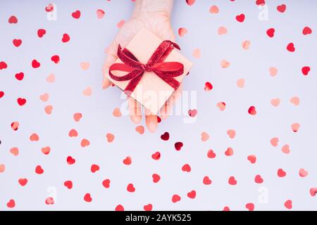 Boîte d'artisanat avec noeud en ruban rouge dans la main femelle. Concept de Saint-Valentin. Décor minimaliste tendance et plat. Horizontal Banque D'Images