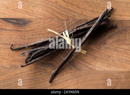 Lot de gousses ou de haricots à la vanille de bourbon secs et attachés sur planche à découper en bois brun, vue sur le dessus Banque D'Images