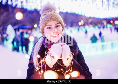 Belle fille en hiver boit thé chaud à partir de verre de carton sur fond de l'éclairage de bokeh du soir Banque D'Images