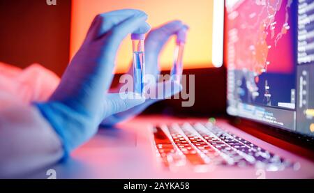 Le personnel infirmier tient le tube de test sanguin dans une combinaison de protection contre les matières dangereuses blanches dans un ordinateur de laboratoire. Étude de concept antidote contre l'épidémie Banque D'Images