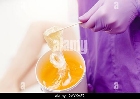 Femme esthéticienne tient la cire de pot de pâte pour l'épilation du sucre shigaring, fond blanc Banque D'Images