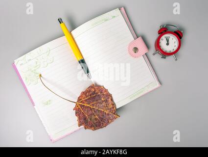 La feuille séchée et le stylo se trouvent sur un ordinateur portable ouvert. Le réveil rappelle l'heure. Bureau. Fournitures scolaires. Placer pour le texte. Vue de dessus. Banque D'Images